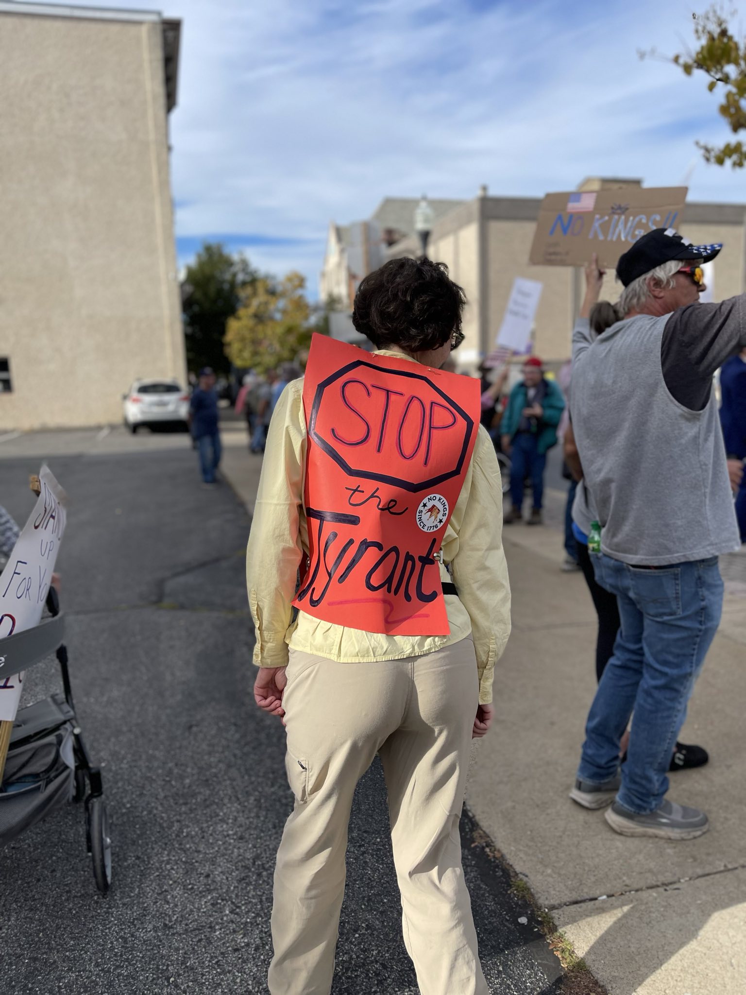 A protester wears a red poster board on their back that says Stop the Tyrant